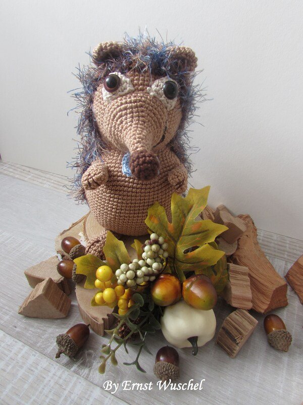 Braunes gehäkeltes Amigurumi-Igel mit flauschigen Stacheln auf Holzscheiben und Herbstdekoration