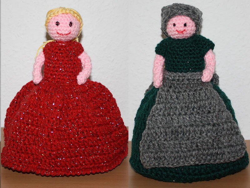 Zwei gehäkelte Amigurumi-Puppen, links rotes glänzendes Kleid, rechts grünes Oberteil mit grauer Schürze
