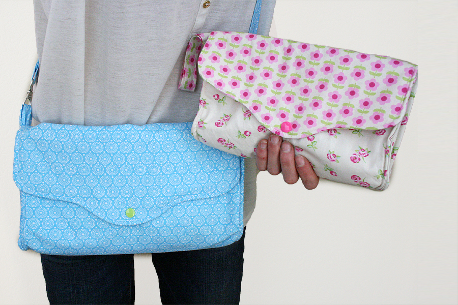 Person trägt blaue Crossbody-Tasche und hält weiße Clutch mit Blumenmuster.