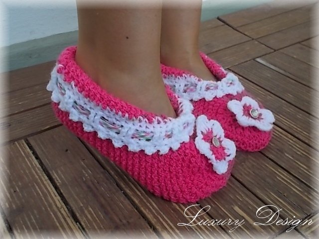 Rosa gestrickte Ballerinas mit weißem Zierrand und Blumenapplikationen mit Knöpfen an Kinderfüßen auf Holzboden