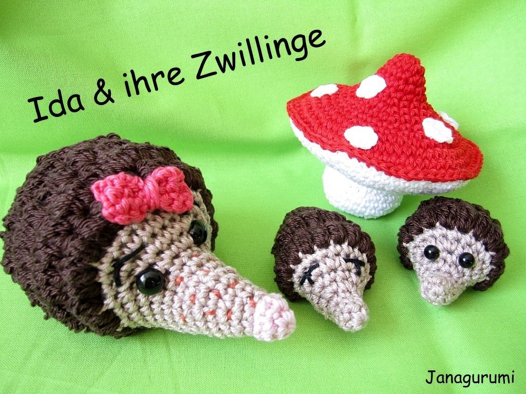 Gehäkelte Igel in drei Größen mit rosa Schleife und ein rot-weißer Fliegenpilz auf grünem Hintergrund