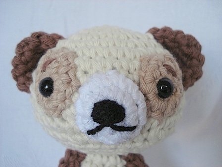 Gehäkelter Amigurumi-Tierkopf in Creme und Braun mit weißer Schnauze und schwarzen Augen