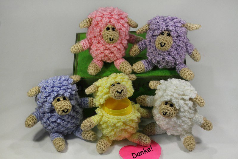 Fünf gehäkelte Amigurumi‑Schafe in Pastellfarben (Rosa, zwei Lilatöne, Gelb, Weiß) mit braunen Gesichtern; gelbes Schaf mit sichtbarer Öffnung und pinkes Herz mit „Danke!“