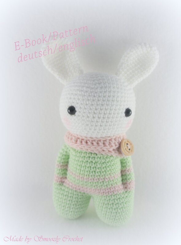 Weißes gehäkeltes Amigurumi-Häschen mit großen Ohren, schwarzen Augen, rosa Bäckchen, mint-rosa gestreiftem Pullover und rosa Schal mit Holzknopf.