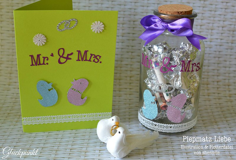 Grüne Hochzeitskarte mit Mr & Mrs Schriftzug neben einem dekorierten Glas mit ähnlicher Beschriftung und zwei weißen Tauben-Figuren