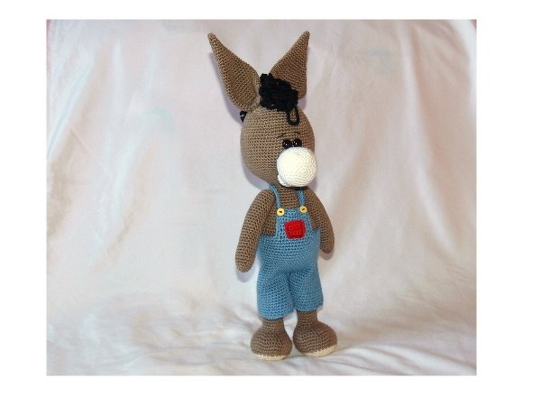 Gehäkelter brauner Amigurumi-Esel mit weißer Schnauze, schwarzer Mähne und blauer Latzhose mit gelben Knöpfen und roter Tasche.