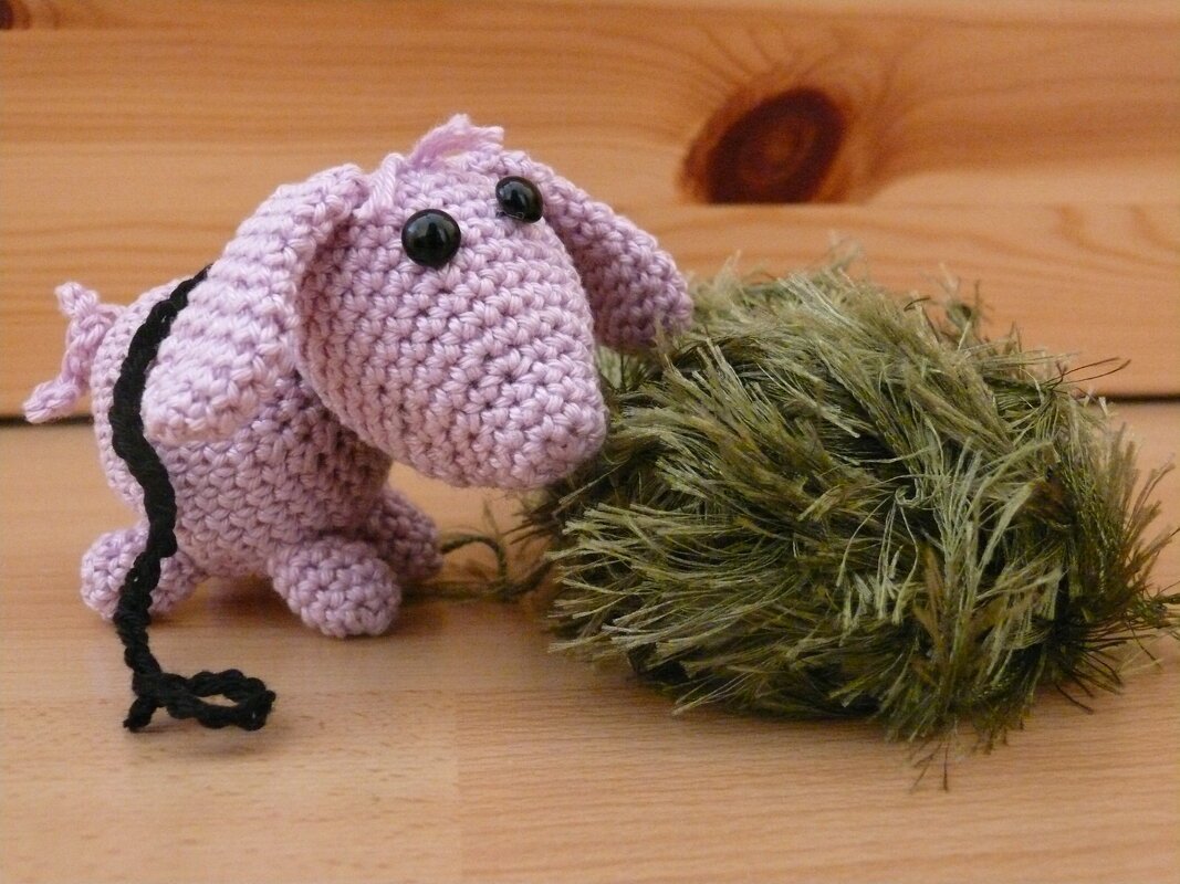 Hellrosa gehäkeltes Amigurumi-Hündchen mit schwarzen Augen neben grünem flauschigem Garnknäuel