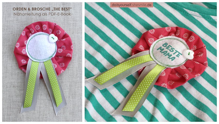 Selbstgenähte rosafarbene Orden-Brosche mit weißem Blumenmuster, grünen und grauen Bändern sowie der Aufschrift BESTE MAMA auf gestreiftem Stoff.