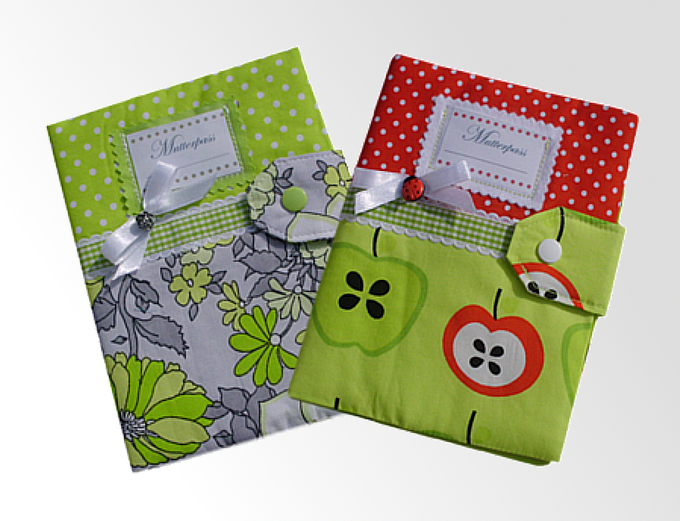 Zwei Stoffhüllen für den Mutterpass: grün-floral mit Punkten und grün mit Apfelmuster und Marienkäferknopf