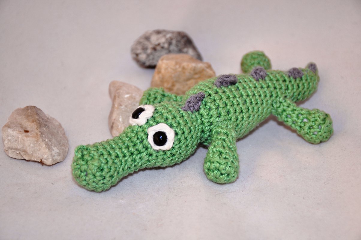 Gehäkeltes grünes Amigurumi-Krokodil mit weißen Augenrändern, liegend