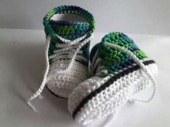 Nahaufnahme gehäkelter Babyschuhe im Sneaker-Design, weiß mit grün und blau