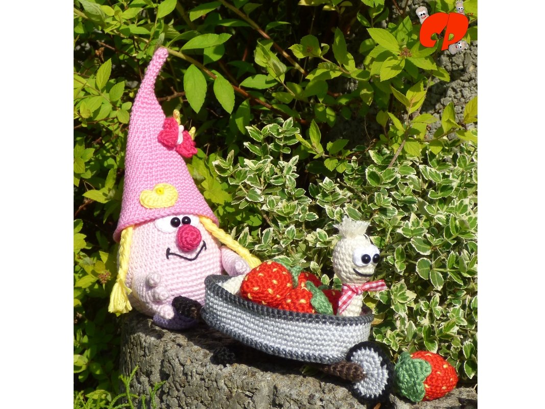 Bunter Amigurumi-Zwerg mit Wagen voller roten Erdbeeren, kleine gehäkelte Raupe mit Halstuch