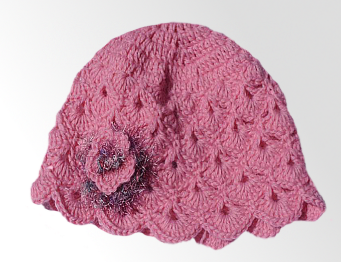 Rosa gehäkelte Babymütze mit Muschelmuster und Blumenapplikation mit leichtem Glitzereffekt an der Seite.