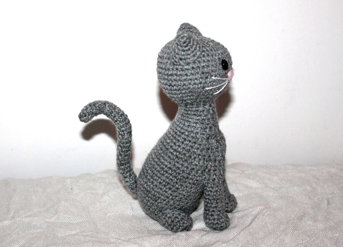 Gehäkelte graue Amigurumi-Katze sitzend seitlich mit gebogenem Schwanz