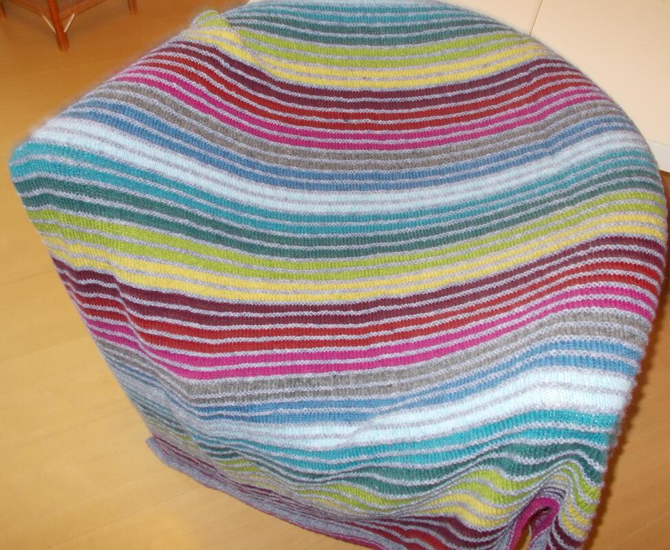 Bunte, gestreifte Strickdecke über einem Möbelstück auf hellem Holzboden.