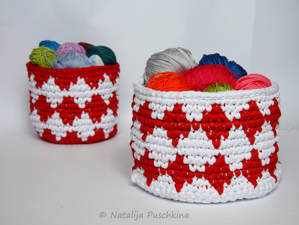 Zwei gehäkelte rot-weiße Körbe mit geometrischem Muster, gefüllt mit bunten Wollknäueln auf weißem Hintergrund