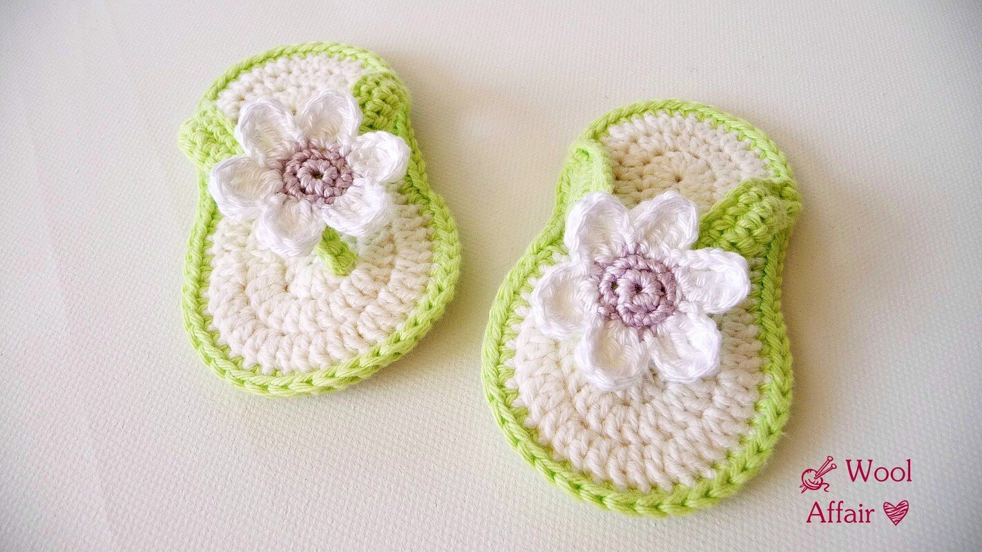 Paar gehäkelter Babysandalen cremeweiß mit grüner Kante und weißer Blüte