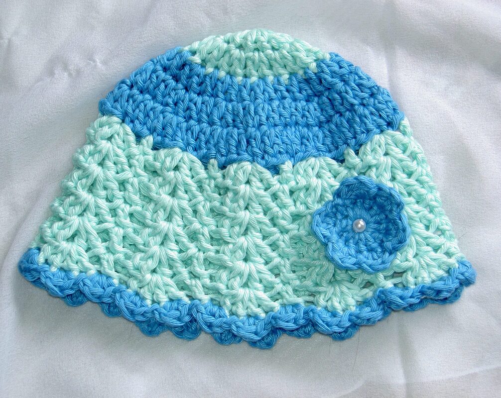 Gehäkelte Babymütze in Mint und Blau mit Wellenrand und kleiner Blume mit Perle.