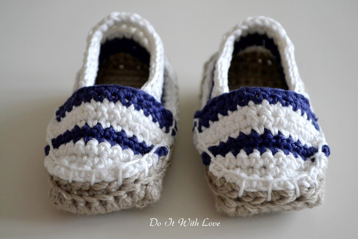 Zwei gehäkelte Babyschuhe weiß mit dunkelblauen Streifen und naturfarbener Sohle
