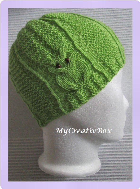 Hellgrüne, gestrickte Mütze mit Eulenmotiv und zwei kleinen braunen Perlen als Augen auf weißem Kopfmodell