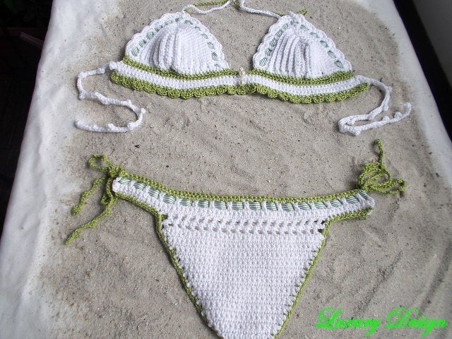 Gehäkelter weißer Bikini mit grüner Borte, liegend auf Sand