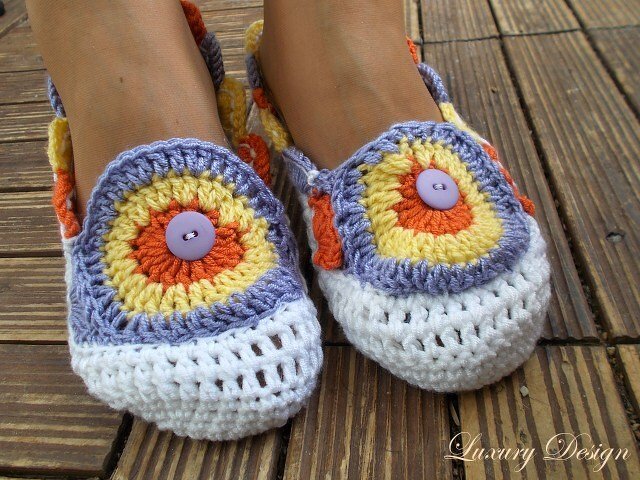 Bunte gehäkelte Ballerina-Hausschuhe mit Granny-Square und Knopf auf Holzboden
