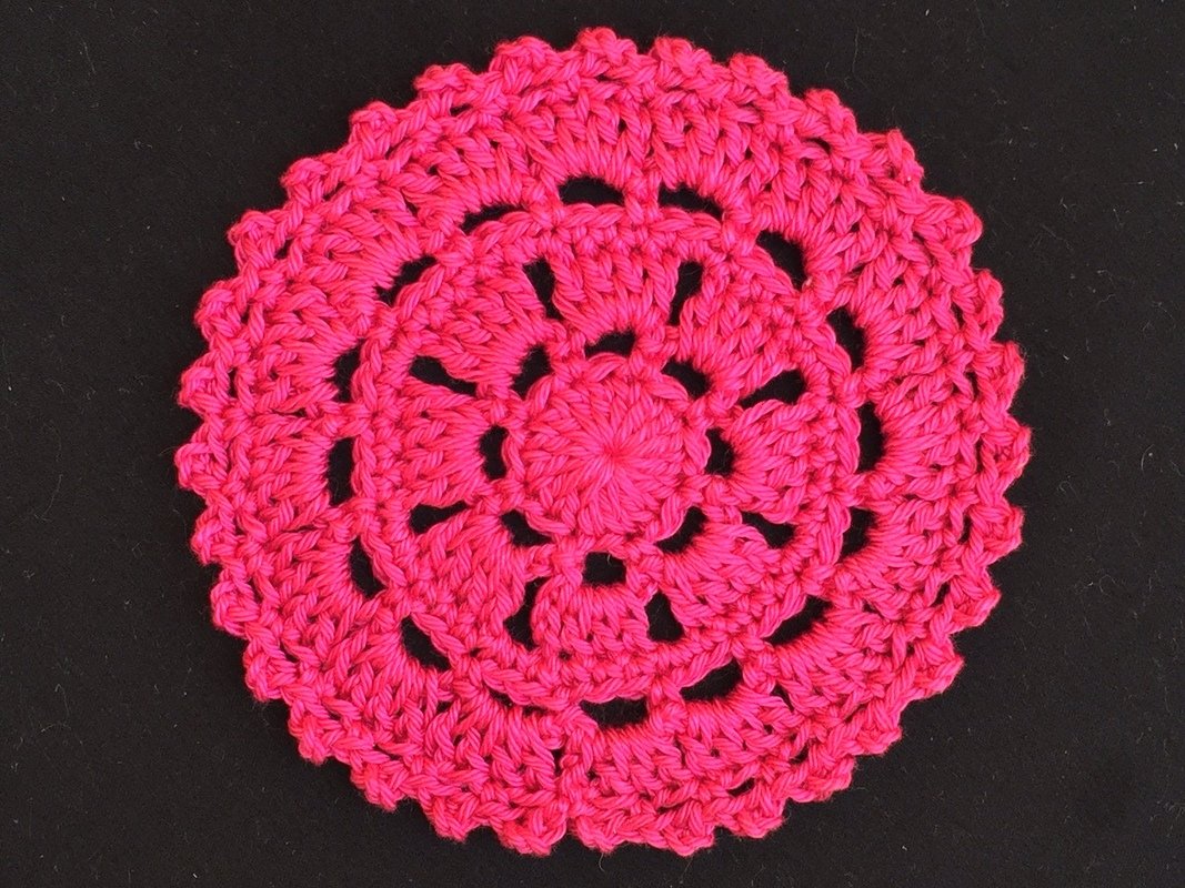 Filigraner, runder Häkeluntersetzer in kräftigem Pink vor schwarzem Hintergrund