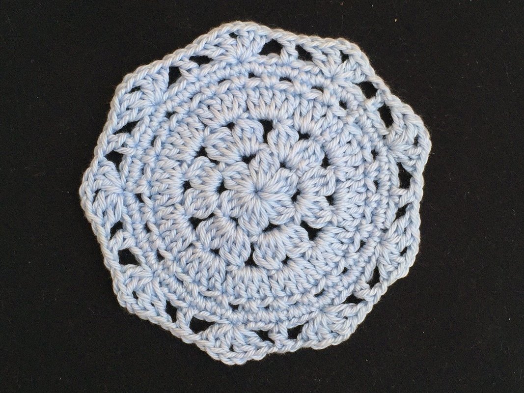 Hellblauer gehäkelter runder Untersetzer mit Blütenmotiv auf dunklem Hintergrund