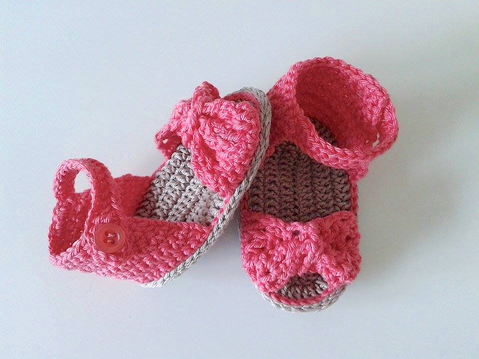 Zwei gehäkelte Babysandalen in Rosa mit beigen Akzenten und Schleifen.