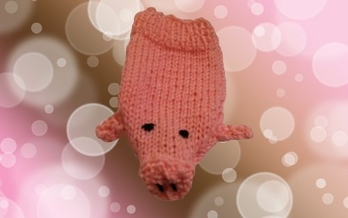 Gestricktes rosa Amigurumi-Schweinchen vor unscharfem, pinken Bokeh-Hintergrund.