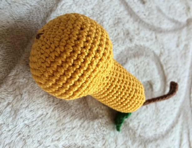 Gehäkelte gelbe Birne mit braunem Stiel und grünem Blatt auf hellem Stoff