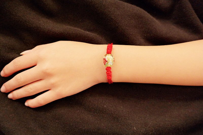 Rotes Kordelarmband mit Blumenperle am Handgelenk