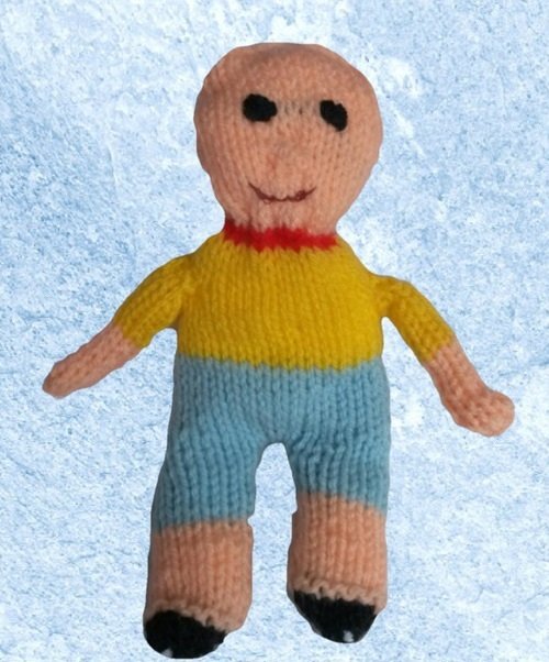 Gestrickte Amigurumi-Puppe mit rundem Kopf, gelbem Oberteil und blauen Hosen vor hellblauem Hintergrund.