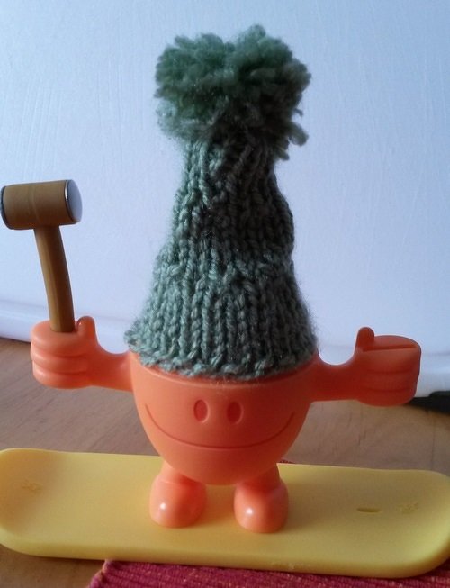 Grüner gestrickter Eierwärmer mit Bommel auf orangefarbenem Eierbecher
