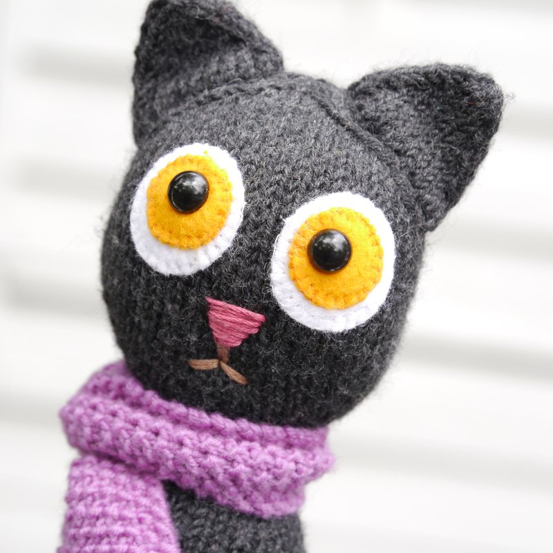 Close-up of crocheted amigurumi cat head showing stitch texture, eye appliqués and purple scarf