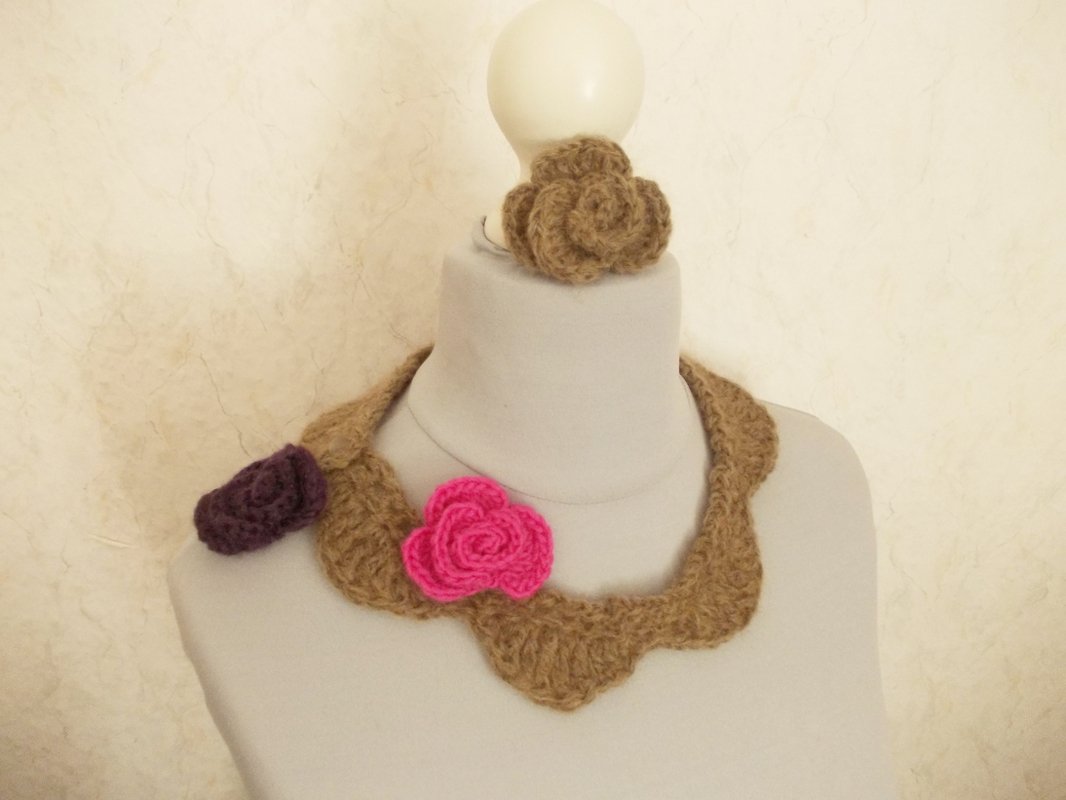 Beiger Muschelkragen aus gehäkeltem Garn mit pinker und lila Rosen-Applikation, auf einer Schaufensterpuppe.
