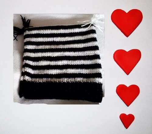 Schwarz-weiß gestreifte Kindermütze mit Rippenbündchen, daneben drei rote Herzen.