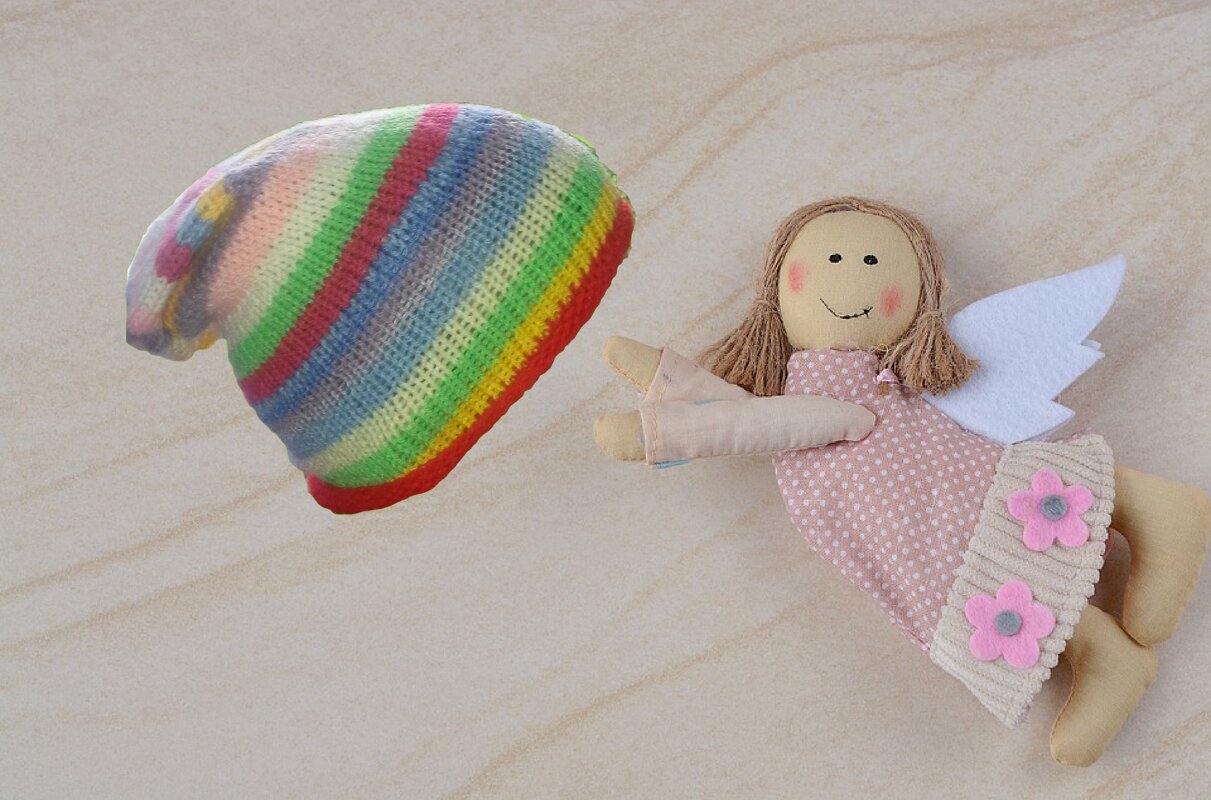 bunte gestrickte Mütze mit Regenbogenstreifen neben einer Stoffpuppe