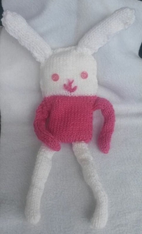 Weißes und pinkes gestricktes Amigurumi-Häschen mit langen Ohren, rosafarbenen Knopfaugen und gestickter Nase auf weißem Untergrund.