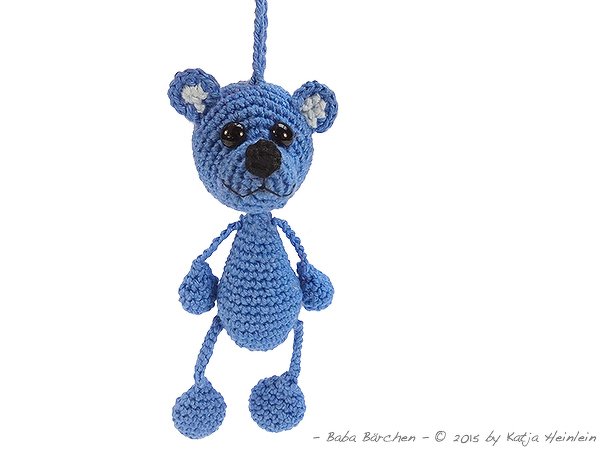 Handgehäkelter blauer Teddybär mit schwarzen Augen an einer Schlaufe hängend