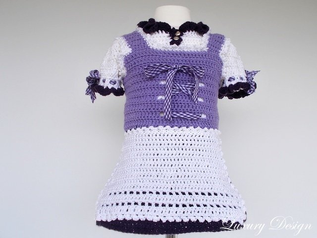 Gehäkeltes Kinderkleid im Trachtenstil in Lila und Weiß mit Schnürband auf Schaufensterpuppe