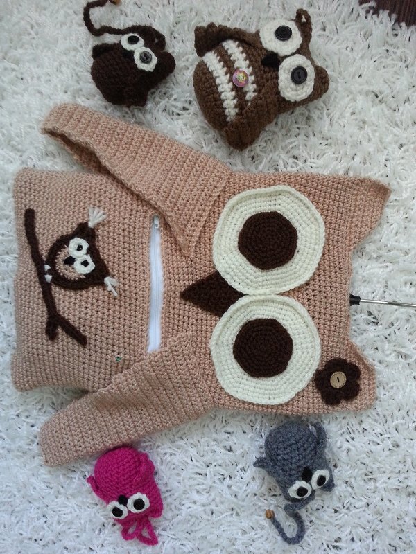 Beiges, handgehäkeltes Eulen-Utensilo mit Reißverschluss und mehreren kleinen gehäkelten Eulen- und Mausfiguren auf weißem Teppich.