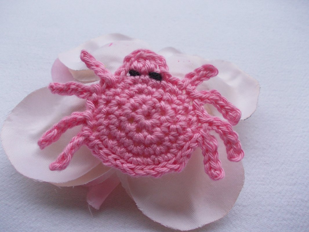 Gehäkelte rosa Spinne mit acht Beinen auf hellrosa Stoffblättern