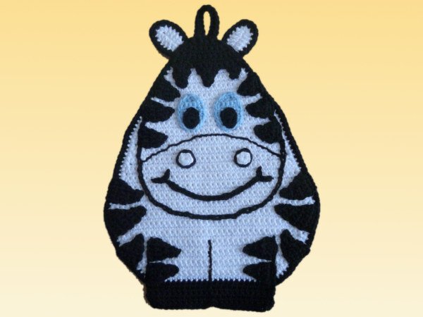 Gehäkelter Topflappen in Zebra-Form, schwarz-weiß mit blauen Augen auf hellem Hintergrund.