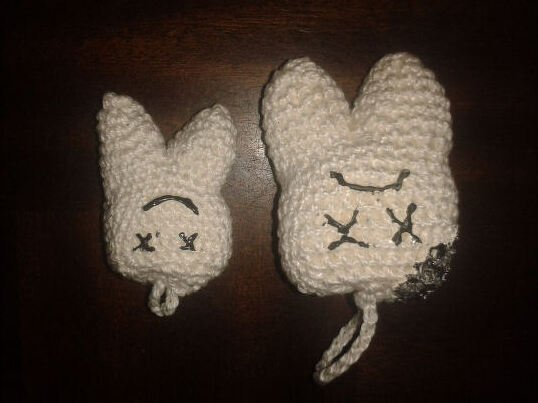Zwei kleine gehäkelte Hasen‑Anhänger in Creme mit gestickten Augen und Schlaufen, einer mit dunkler Verfärbung