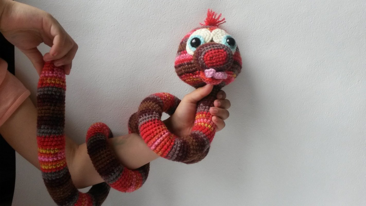 Bunte gehäkelte Amigurumi-Schlange mit großen Augen um einen Arm gewickelt