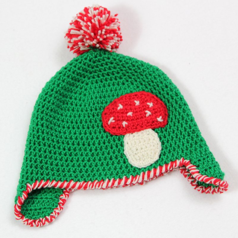 Grüne gehäkelte Ohrklappenmütze für Kinder mit rotem Pilz-Applikation und rot-weißem Bommel