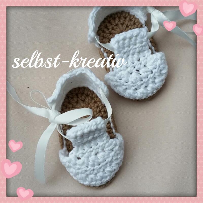 Zwei gehäkelte Babyschuhe in Weiß und Beige mit Schleifen, Draufsicht