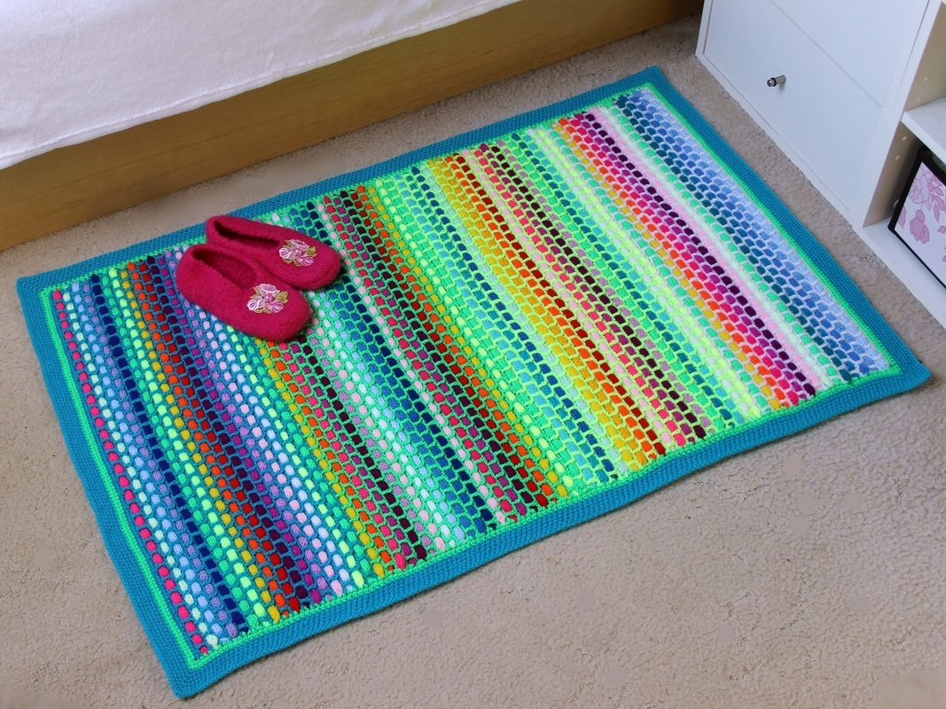 bunter häkelteppich mit türkiser einfassung und rosa hausschuhen