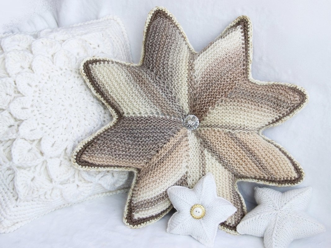 Gestricktes sternförmiges Kissen in Beige mit Zierknopf, arrangiert mit zwei weißen Sternkissen auf hellem Hintergrund